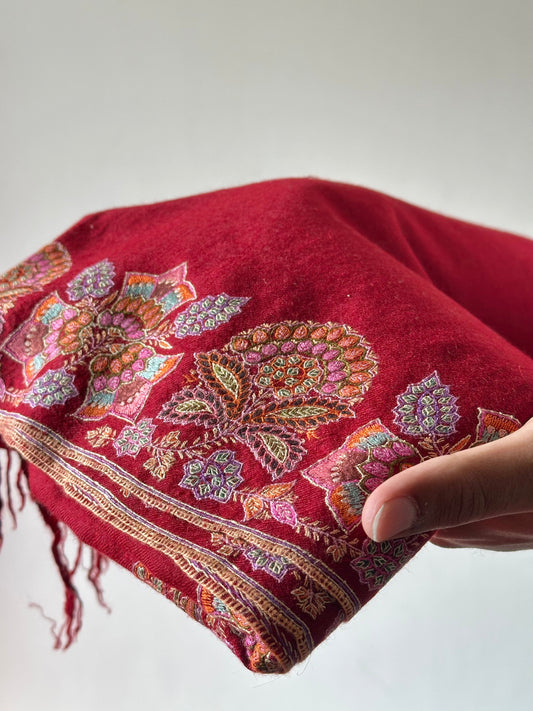 Red embroidered fabric held by a hand against a neutral background